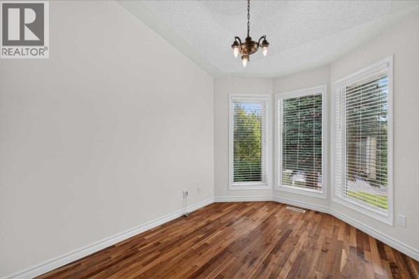 Empty room with hardwood floors and three large bay windows overlooking greenery. - 21 Strathearn Gardens Sw, Calgary