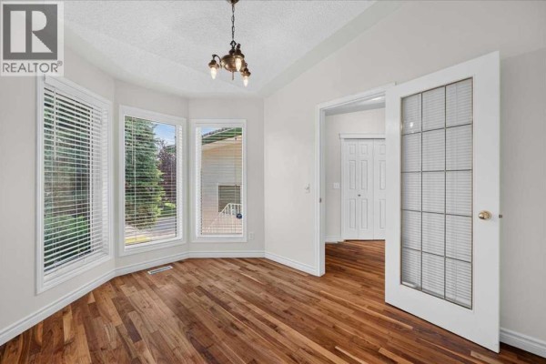Bright room with hardwood floors, bay windows, and double doors leading to a hallway. - 21 Strathearn Gardens Sw, Calgary