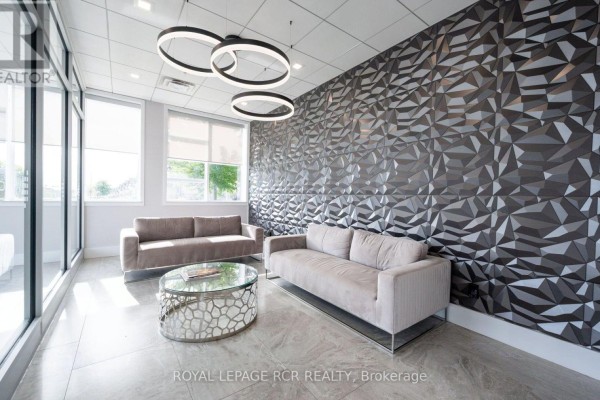 Lobby seating area with two velvet sofas, a glass coffee table, and a striking geometric wall. - 210 - 105 Spencer Avenue, Orangeville