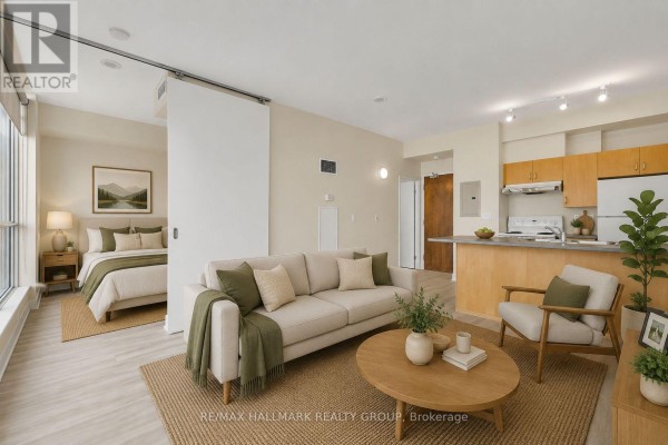 Open-concept living area with a sofa, armchair, coffee table, and a partially visible bedroom. - 210 - 180 York Street, Ottawa
