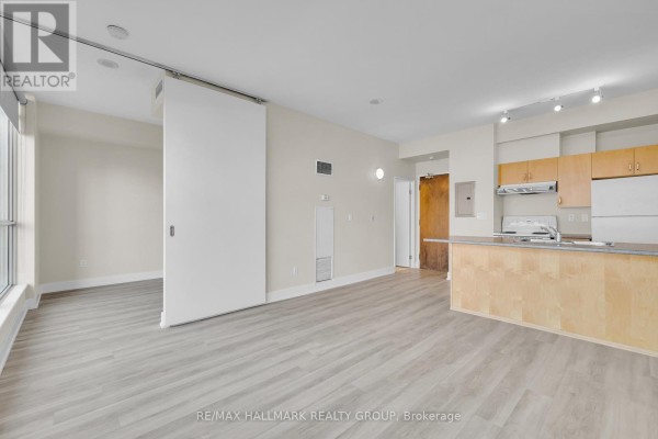 Living area and kitchen with light wood cabinets, a peninsula, and a sliding door to a bedroom. - 210 - 180 York Street, Ottawa