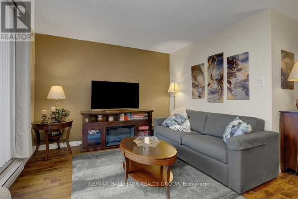 Living room with grey sofa, coffee table, entertainment unit, and hardwood floors. - 210 - 2000 Jasmine Crescent, Ottawa