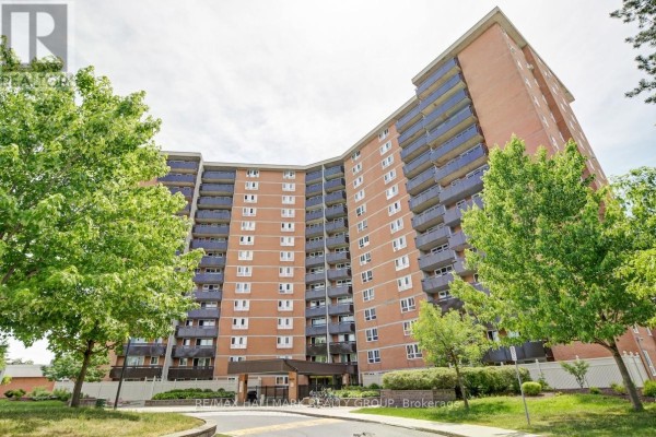 Exterior view of a tall brick apartment building with balconies and trees. - 210 - 2000 Jasmine Crescent, Ottawa