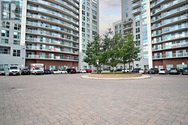 Courtyard area with paved ground, trees, and parked cars in front of apartment buildings. - 210 - 2152 Lawrence Avenue E, Toronto