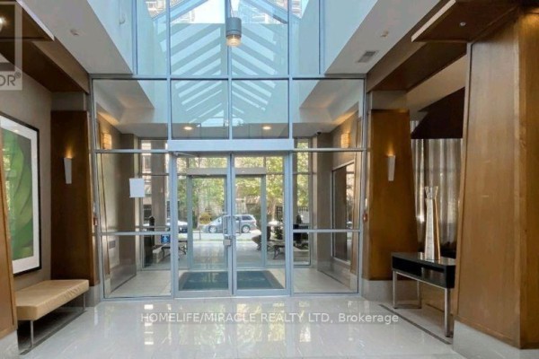 Apartment building lobby with glass doors, seating, and wood paneling. - 210 - 31 Bales Avenue, Toronto