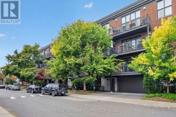 Exterior of apartment building with brick facade, balconies, and a garage entrance on a tree-lined street. - 210 - 457 Mcleod Street, Ottawa