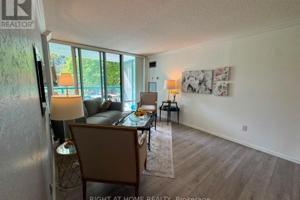 Spacious living room with light grey walls, light wood flooring, sofa, armchairs, and wall art. - 210 - 7250 Yonge Street, Vaughan