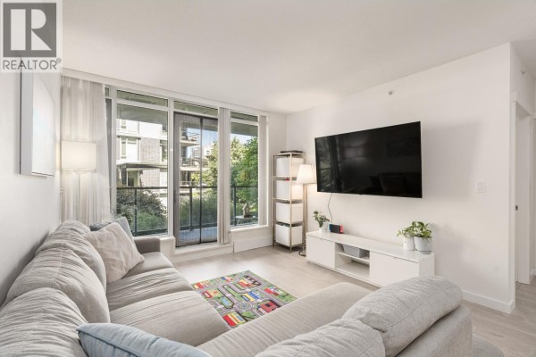 Living room featuring a grey sectional sofa, mounted TV, and floor-to-ceiling windows. - 210 3168 Riverwalk Avenue, Vancouver