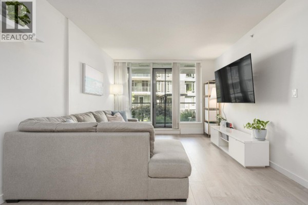 Living room showing a grey sofa, entertainment unit, television, and balcony doors. - 210 3168 Riverwalk Avenue, Vancouver