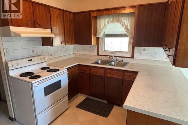 Corner of the kitchen featuring a white stove, double sink, and wood cabinetry. - 210 Alexander Avenue, Canora