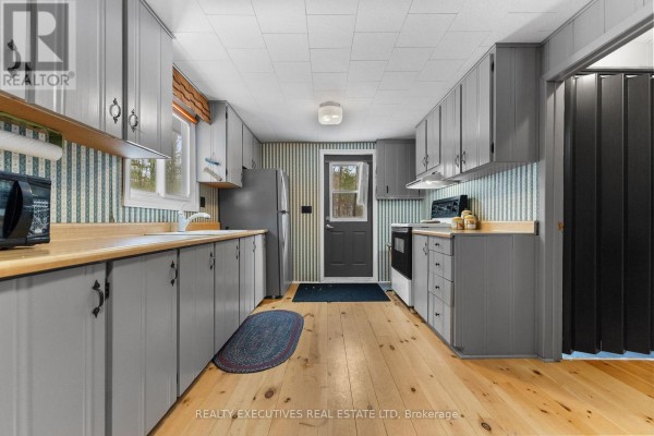 View from kitchen into dining and living area with wood stove and chairs. - 210 Birch Bay Lane, Tay Valley