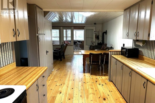 Living area with wood stove, dining table, chairs, and view into sunroom. - 210 Birch Bay Lane, Tay Valley