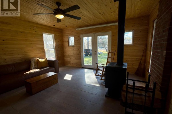 Living area with wood-paneled walls, a brown sofa, rocking chairs, and a wood stove. - 210 C Storms Road, Prince Edward County