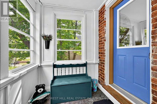 Sunroom with white wainscoting, large windows, and a green storage bench in front of a blue door. - 210 Centennial Drive, Midland