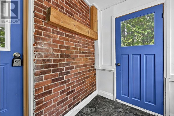 Interior sunroom with exposed red brick wall, wooden beam, and a blue door. - 210 Centennial Drive, Midland