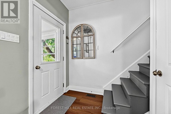 Interior view of a doorway with a white door, a mirror with an arched frame, and grey stairs. - 210 Centennial Drive, Midland