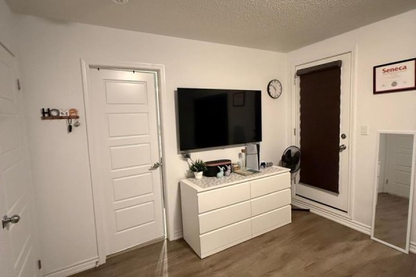 Bedroom with white dresser, mounted television, and door leading outside. - 210 Keppel Circle, Brampton