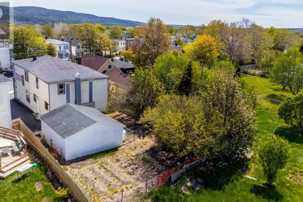 Rear exterior of the building showing a detached garage and overgrown yard area. - 210 Pennywell Road, St  John S