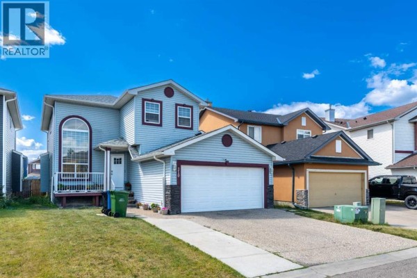 Exterior view of the light blue two-story house with a garage and gravel driveway. - 210 Taracove Landing Ne, Calgary
