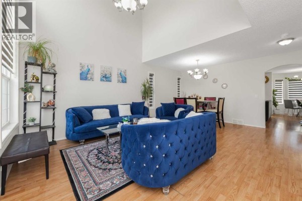 Living room with vaulted ceiling, blue velvet sofas, glass coffee table, and hardwood floors. - 210 Taracove Landing Ne, Calgary