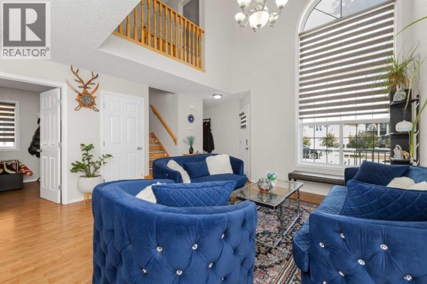 Living room with vaulted ceiling, blue velvet sofas, wood-burning fireplace, and stairs to the second floor. - 210 Taracove Landing Ne, Calgary