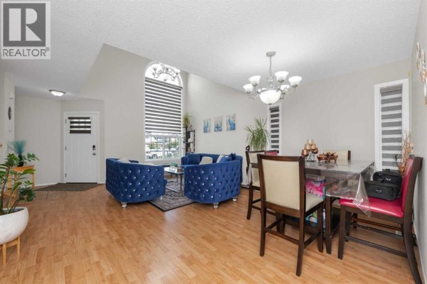 Living and dining area with hardwood floors, a large window, and furniture for seating and dining. - 210 Taracove Landing Ne, Calgary