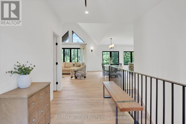 Hallway with light wood floors and a railing overlooking an open-concept living and dining area. - 210 White Valley Road, Trent Lakes