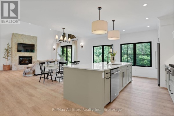 Open-concept kitchen and living area with a large island, stone fireplace, and large windows. - 210 White Valley Road, Trent Lakes