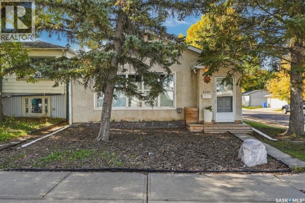 Front exterior view of the stucco house with trees and a street view on the right. - 2100 Lindsay Street, Regina