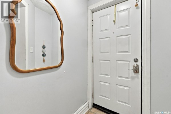 Interior view of the front entrance with a white door, a mirror, and light gray walls. - 2100 Lindsay Street, Regina