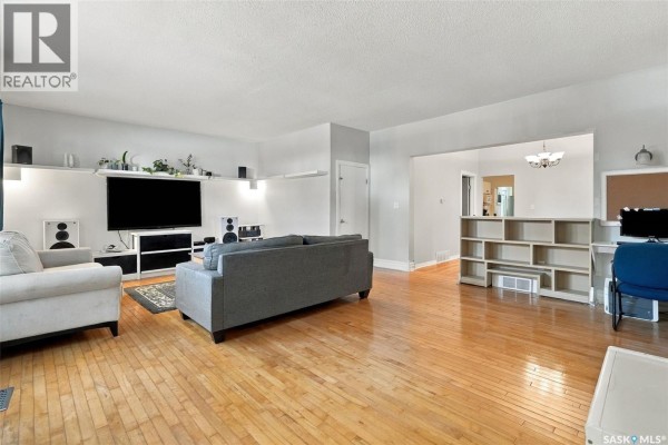 Living room with hardwood floors, a large television, gray sofa, and open doorway to dining room. - 2100 Lindsay Street, Regina