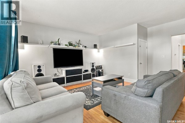Living room with hardwood floors, two gray sofas, a coffee table, and media console. - 2100 Lindsay Street, Regina