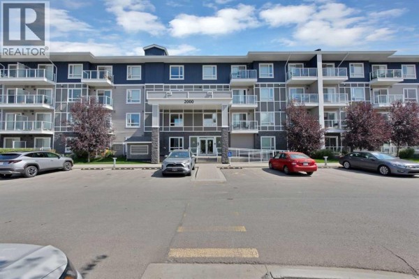 Exterior of the apartment building with balconies, parking lot, and cars. - 2101, 76 Cornerstone Passage Ne, Calgary