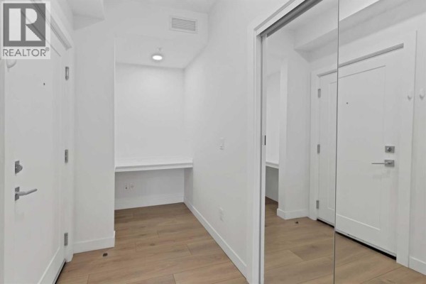 Interior hallway with white walls, hardwood floors, and a mirrored closet door. - 2101, 76 Cornerstone Passage Ne, Calgary