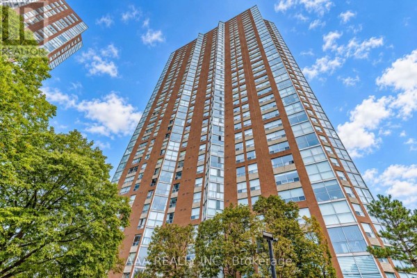 View looking up at a tall brick apartment building with many windows under a blue sky. - 2101 - 5 Concorde Place, Toronto