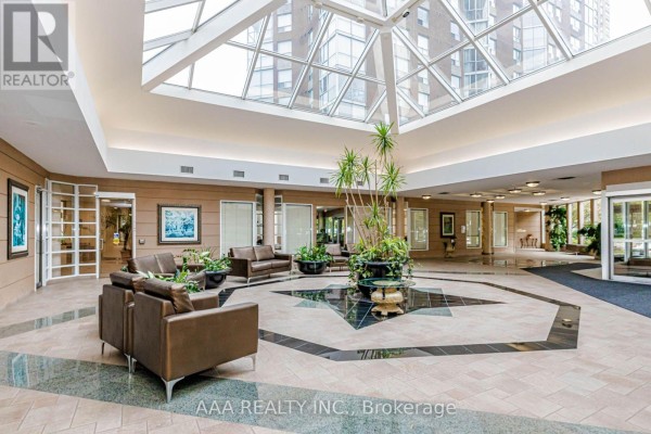 A large, bright atrium lobby with a glass ceiling, tile floors, and leather seating areas. - 2101 - 5 Concorde Place, Toronto