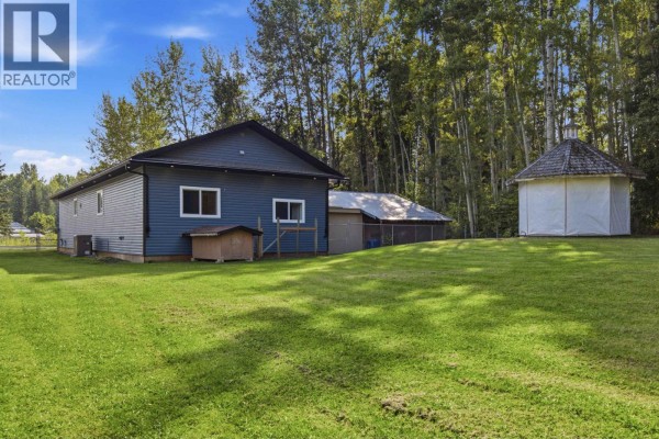 Exterior view of the blue mobile home with a covered entryway and surrounding trees. - 2102 Quartz Road, Quesnel