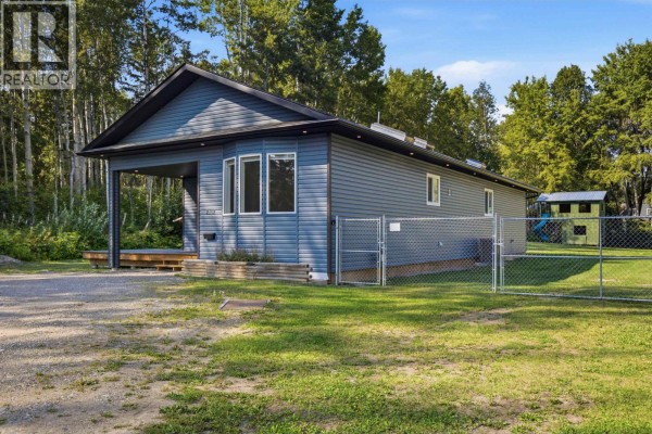 Backyard view with a grassy lawn, children's play structure, shed, and RV. - 2102 Quartz Road, Quesnel