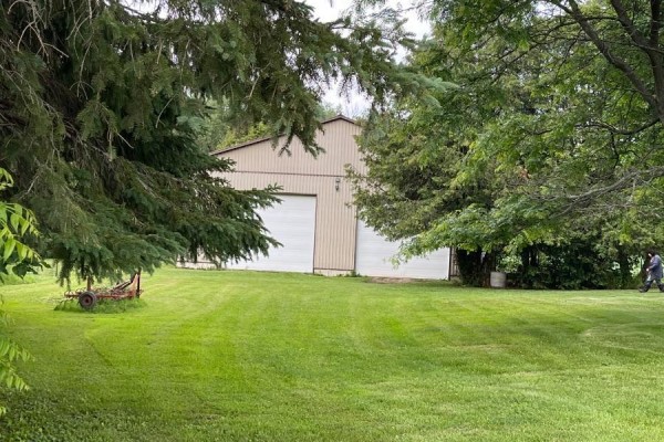 Exterior of a beige barn with large white garage doors set in a grassy yard. - 21021 Cherry Hill Road, Thames Centre