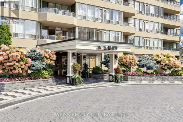 Close-up of the building entrance with decorative planters, columns, and a covered walkway. - 2104 - 10 Torresdale Avenue, Toronto
