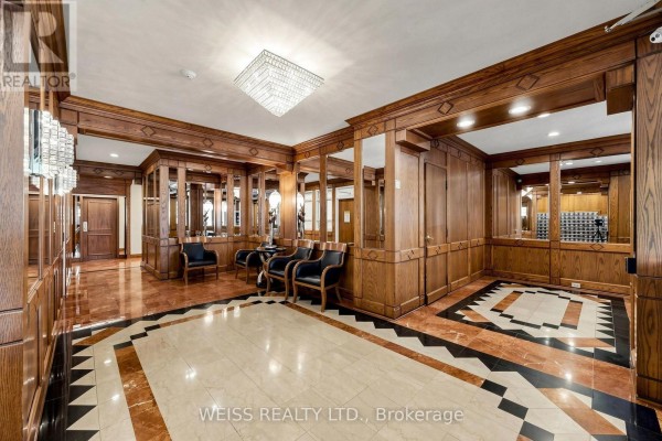 Apartment building lobby with marble floors, dark wood paneling, mirrored walls, and seating. - 2104 - 10 Torresdale Avenue, Toronto