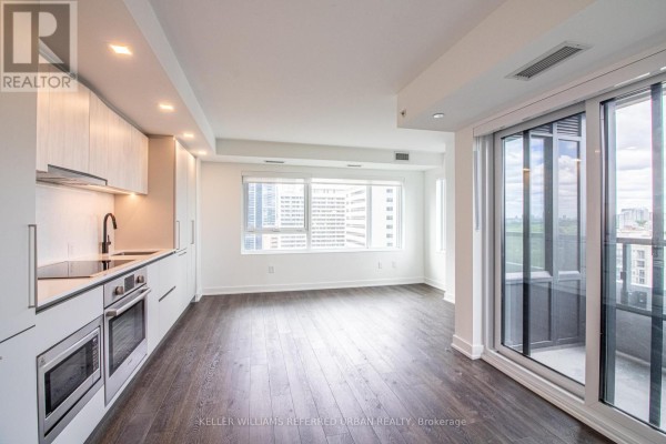 Empty living and dining area with a modern kitchen, dark wood floors, and large windows. - 2104 - 609 Sherbourne Street, Toronto