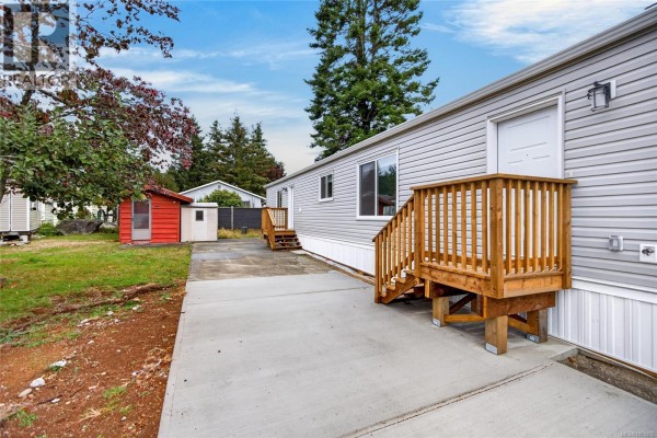 Close-up of the mobile home's light gray siding, wooden stairs, and white front door. - 2104 Pemberton Pl, Comox