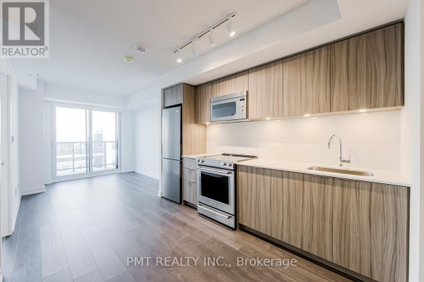 Modern apartment kitchen with light wood cabinets, stainless steel appliances, and dark wood floors. - 2105 - 30 Samuel Wood Way, Toronto