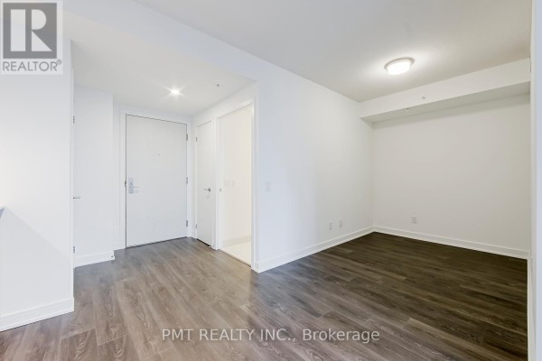 Empty room with white walls, dark wood floors, and a hallway leading to two doors. - 2105 - 30 Samuel Wood Way, Toronto