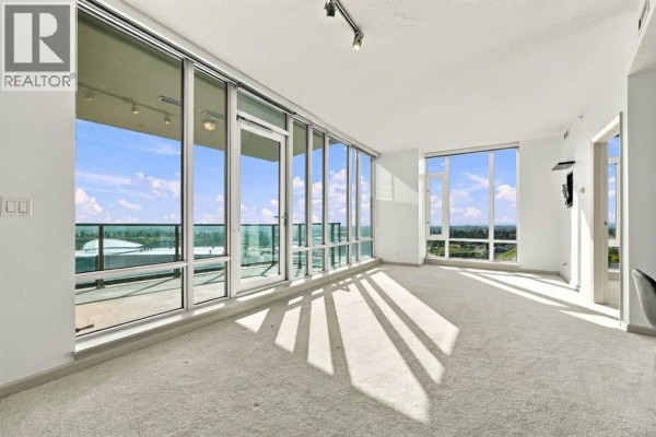 Spacious living area with cream carpet and wall-to-wall windows offering city views. - 2106, 210 15 Avenue Se, Calgary