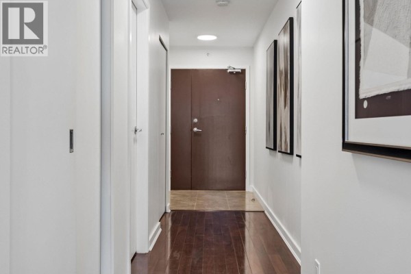 Interior hallway with white walls, dark wood floors, and a brown door. - 2106 918 Cooperage Way, Vancouver