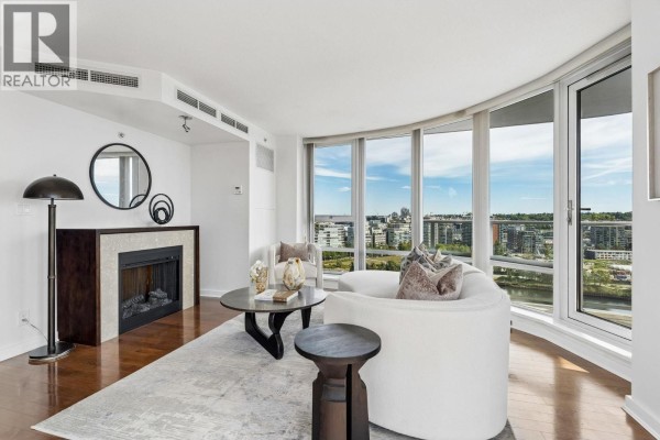 Living room with fireplace, curved windows, white sofa, and city views. - 2106 918 Cooperage Way, Vancouver