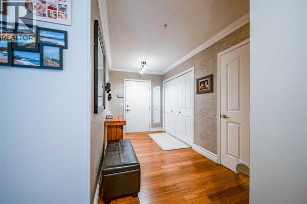 Hallway view showing hardwood floors, textured wallpaper, white doors, and a leather bench. - 2107, 20 Harvest Rose Park Ne, Calgary