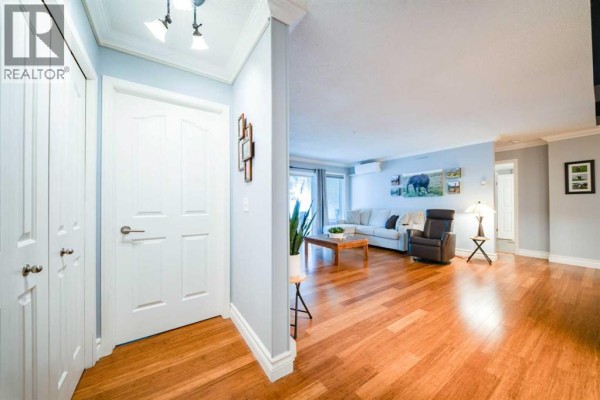 View from the entryway into the living room with hardwood floors and light blue walls. - 2107, 20 Harvest Rose Park Ne, Calgary